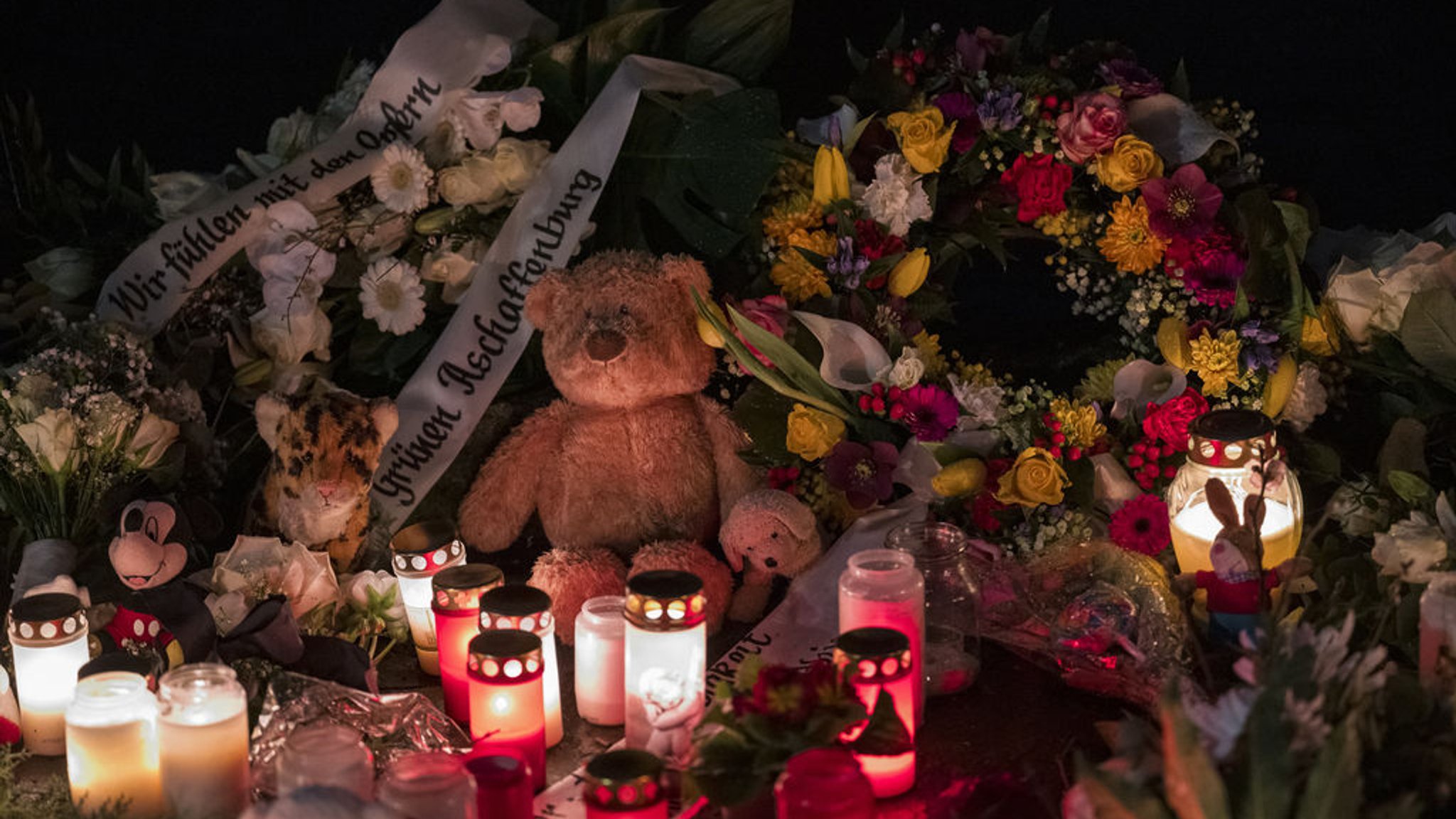 ARCHIV - 24.01.2025, Bayern, Aschaffenburg: Ein Teddybär liegt neben Blumenkränzen und Kerzen auf dem Boden und erinnert an den tödlichen Messerangriff. Zahlreiche Kerzen und Kuscheltiere erinnern am Freitagmorgen im Park Schöntal an die Opfer der tödlichen Messerattacke. (zu dpa: «Fast eine halbe Million für Betroffene der Messerattacke») Foto: Daniel Vogl/dpa +++ dpa-Bildfunk +++